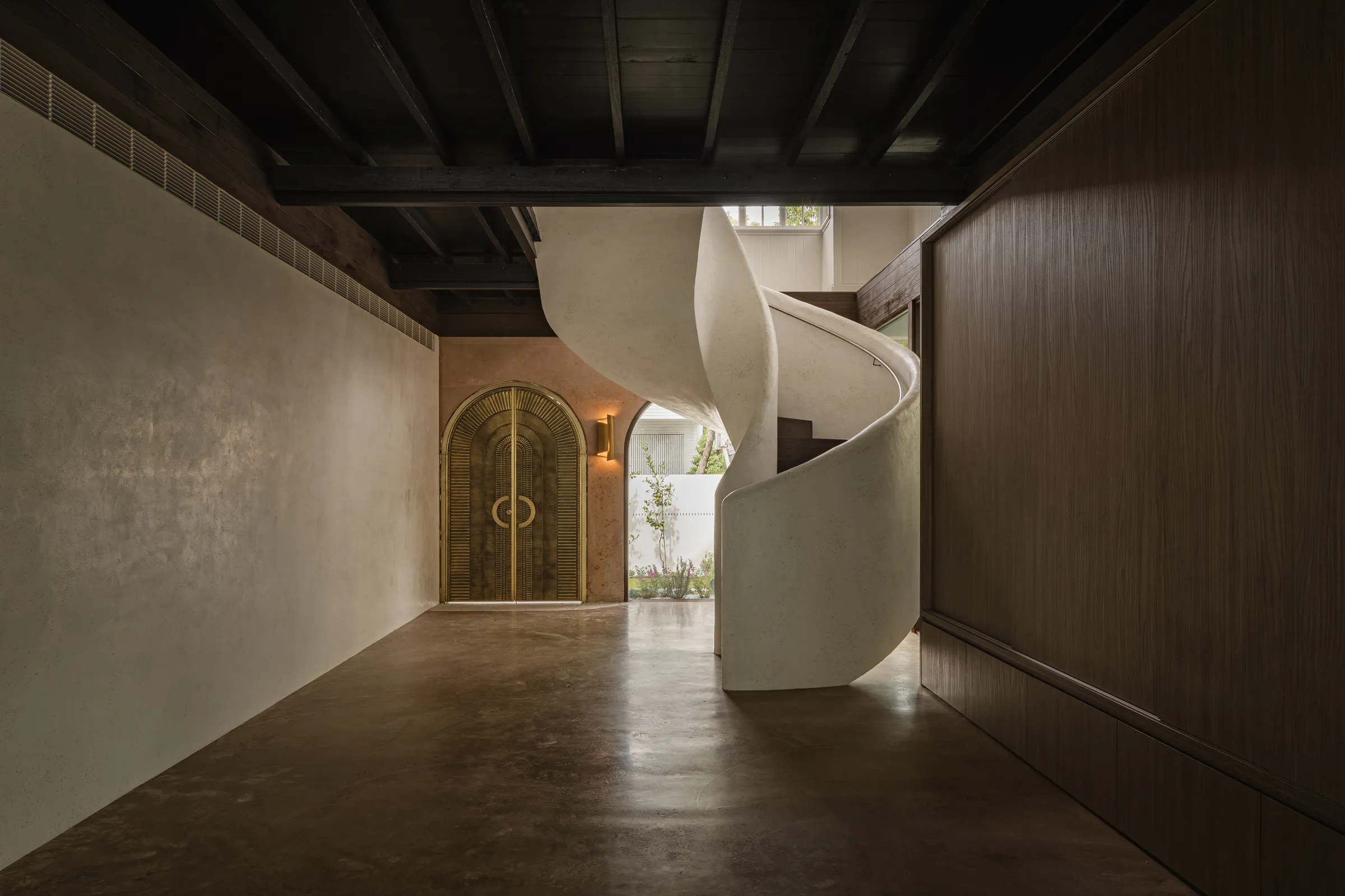Sculptural hand-burnished plaster spiral staircase rising from a polished concrete hallway — Mark Street, Brisbane.